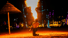A man performing fire tricks on the beach at night.
