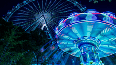 A brightly lit fairground features a carousel and a large Ferris wheel against a dark sky.