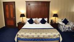 Premium Rooms at The Bristol Hotel Gurgaon, with a large bed, spreads, pillows, lamps, a door, and a cushion.
