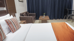Side view of the Executive Room at Sarovar Portico, Bhubaneswar, highlighting the plush double bed with orange accents, a seating area with a centre table, and closed curtains.