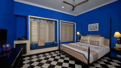 Vibrant blue hotel room at the Old Court House by Abad, with a four-poster bed and checkered floor, perfect for a stay near Fort Kochi beach.