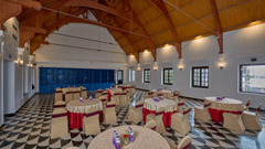 Spacious banquet hall at, The Old Court House by Abad, a business hotel in Kochi, featuring round tables, chequered floors, and an open wooden truss ceiling.