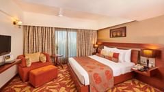 Room at Pride Premier Nagpur featuring a plush bed with lamps on the both sides on nightstands and a TV mounted in front o the bed