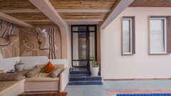The welcoming entrance to the Two Bedroom Villa With Private Pool, featuring a stylish facade with clean lines and large glass doors. A covered patio with natural wooden beams and comfortable outdoor seating suggests a tranquil space for relaxation before 