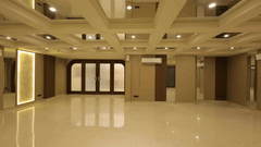 A large, empty banquet hall at Tulip Inn Gurugram with polished white floors, wood-panelled walls, and a multi-level recessed ceiling with warm lighting.