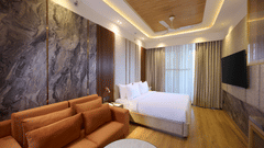 Wide view of a Tulip Inn Gurugram room showing a large sofa in the foreground and a plush bed by the window.