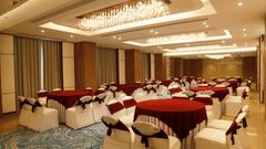 A banquet hall in Zirakpur with round tables, carpeted floors, and warm lighting - Tulip Inn, Zirakpur