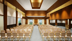 A well-lit event hall with chairs arranged neatly facing a central stage, featuring modern wooden interiors, windows offering natural light, and a sleek, polished floor - Uday Backwater Resort