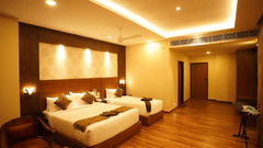 A corner angle of family room with two beds that is king size bed and single bed, several pillows, a chair, a table, wooden floor, ceiling fan, lighting, and an entrance area at V FIVE HOTEL