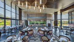 Indoor dining area at Vandhara Sarovar Premiere, Patkote, showing set tables, chairs, and high ceilings with large cylindrical light fixtures.