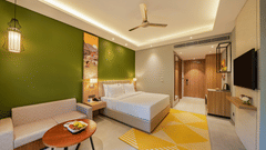 A Deluxe Room at Vandhara Sarovar Premiere, Patkote, with a green accent wall, double bed, upholstered sofa, and a geometric patterned rug.