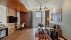 A suite at Vandhara Sarovar Premiere, Patkote, showing a living area with a patterned rug, wooden wall paneling, and a wall-mounted TV.