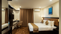 An elegant bedroom at VITS Select, Bengaluru, featuring a plush bed, rich wall paneling and curtains, a reflective mirrored surface, and a mounted air-conditioning unit for the perfect stay in Bengaluru.