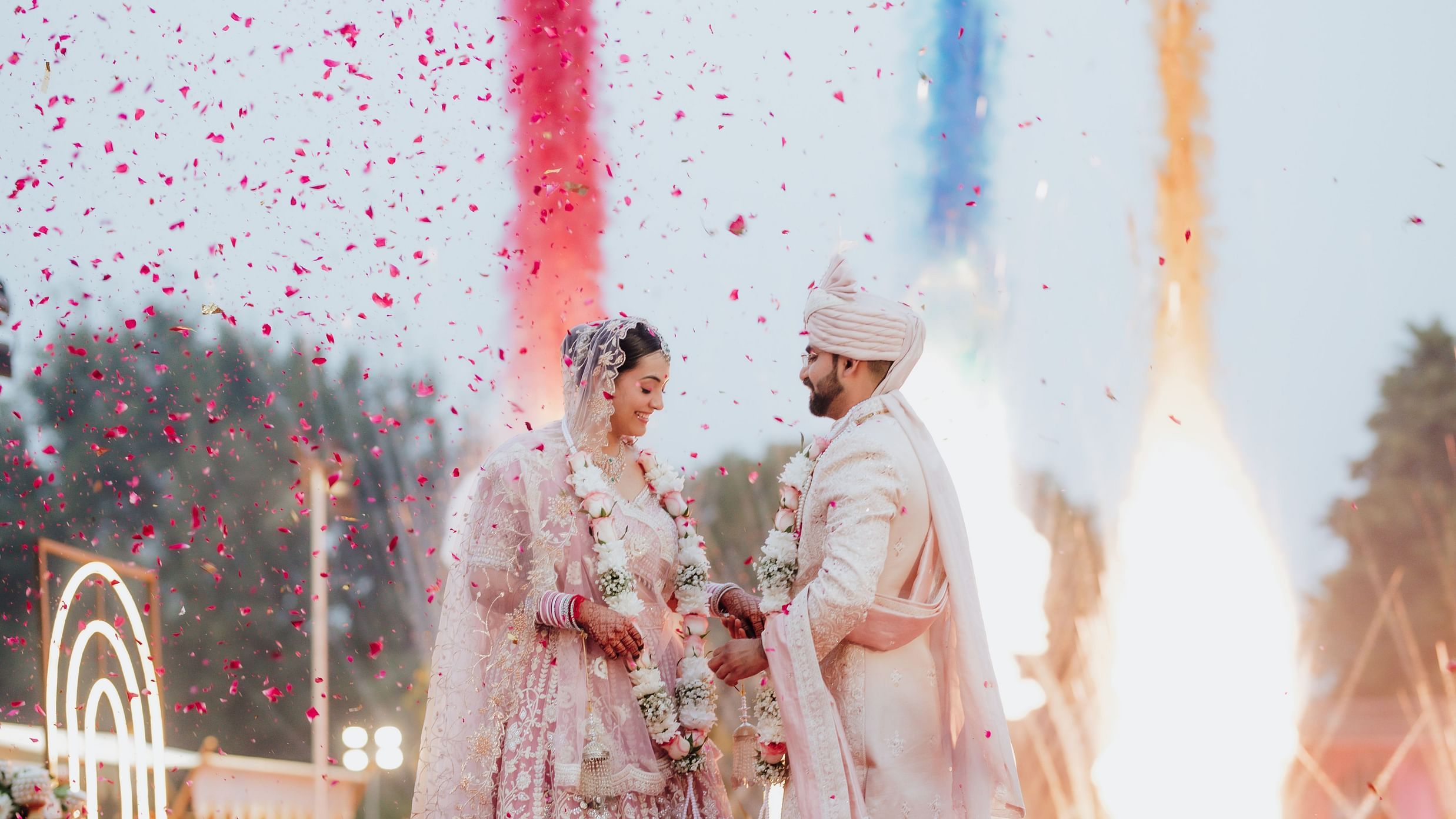 Bride and groom exchanging garlands under colorful smoke effects during the wedding ceremony.