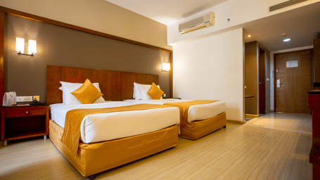 Twin bed room at Featherlite Evoma Hotel with beds dressed in white and gold linen and light wooden flooring throughout the whole room.