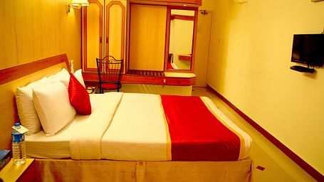 a side view of a room furnished with a comfortable bed, television, wardrobe and looking glass - Hotel Swagath, Bangalore