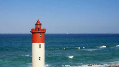 A view of a lighthouse near the Best Beach in Kovalam with a clear sky in the background where waves can be seen hitting the shore