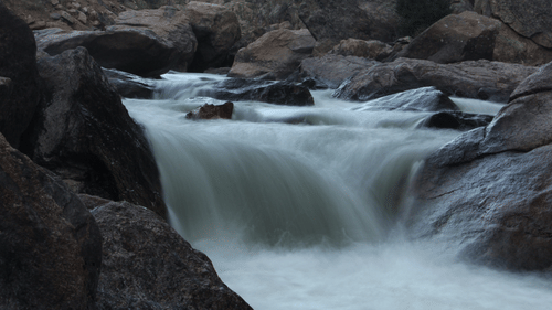 An overview of a river flowing through many rocks with trees in the background