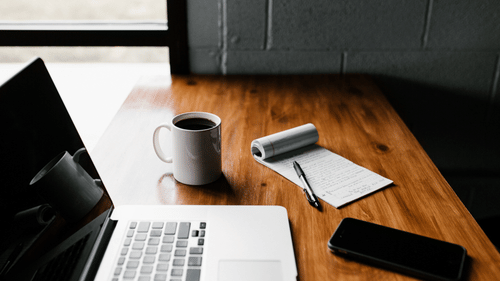 laptop on wooden table next to a mug of coffee 