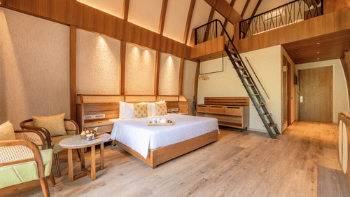 an interior of a bamboo villa with a king size bed and a stairs to the second deck at Ananta Spa and Resort, Ajabgarh