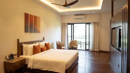 Spacious bedroom with seating area, bedside table, a wall-mounted TV, wooden flooring, and a balcony view at Ananta Spa and Resort, Ajabgarh.