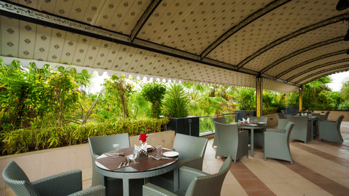 Open restaurant with roof on top featuring several sets of dining table and chairs at Arawali Ananta ELite, Ranakpur.