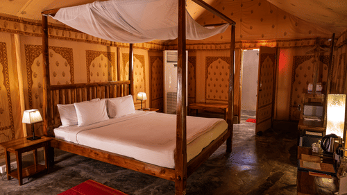 A room with a wooden 4-poster bed with 2 bedside lamps against patterned walls and a small work desk opposite to it at Barefoot at Havelock.