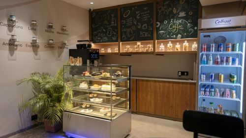 A well-stocked cafe counter with display cases of pastries and beverages, ready for service - Biznotel By Pride Surat