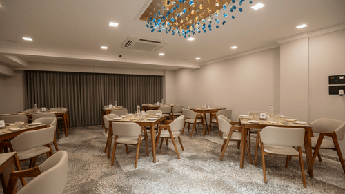 A bright, contemporary restaurant space with wooden tables and chairs, illuminated by a decorative ceiling light - Biznotel By Pride Surat