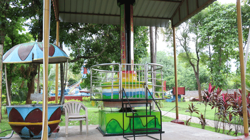 A colourful amusement ride with a spinning seat surrounded by metal fencing, set in a lush green outdoor area atBlack Thunder, Coimbatore