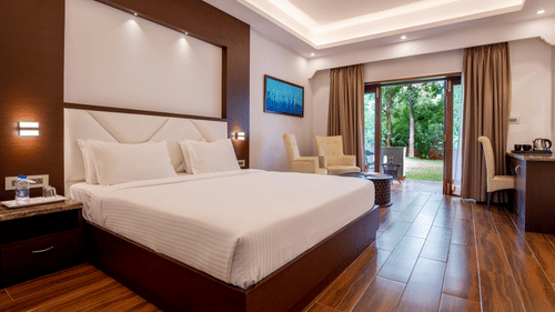 A modern bedroom with a large bed, wooden flooring, stylish decor, and wide windows offering views of nature outside - Black Thunder, Coimbatore