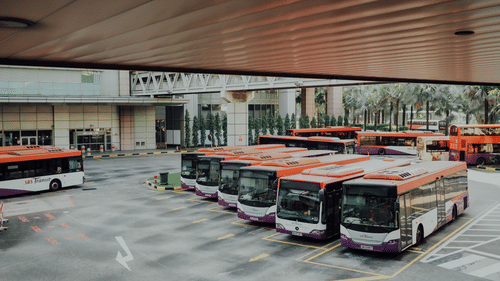 buses parked next to each other in a bus depot as seen from a distance.