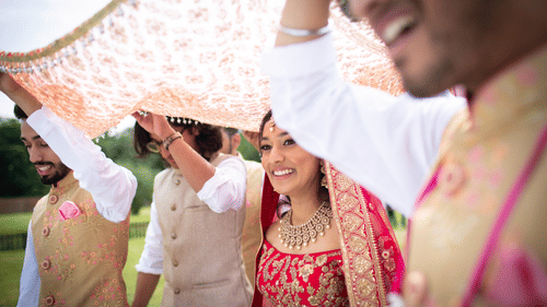 A group of people smiling and holding a cloth above a couple in a traditional wedding ritual.