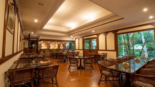 An indoor seating area of a restaurant with wicker chairs and tables, warmly lit with large windows offering a view outside - Black Thunder, Coimbatore