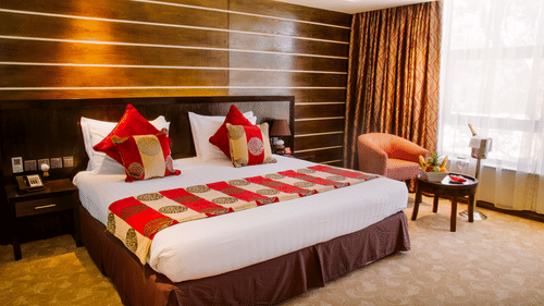 Superior Double Room at Boma Inn Eldoret featuring a double size bed, a sofa chair with centre table, bedside table on either side, and a window with curtain.