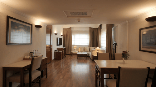 A wide view of the living and dining space with wooden flooring, elegant furniture, wall art, and ambient lighting in the Executive Suite at Clarks Amer, Jaipur.