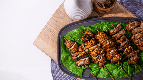 Plate of grilled skewered kebabs served on banana leaves.