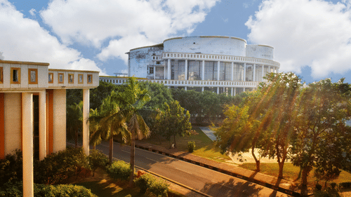A wide-angle view of a large, circular white building with tall pillars and a manicured lawn under a blue sky with scattered clouds.
