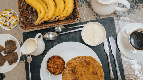 A traditional Indian breakfast tray with stuffed paratha, curd, bananas, and hot tea, presented with thoughtful detail for a hearty start at Colonel’s Retreat.