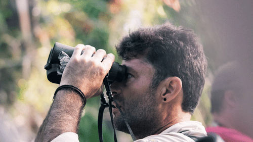 A man uses binoculars for birdwatching in a wooded area near Heritage Village Resorts & Spa, Goa.