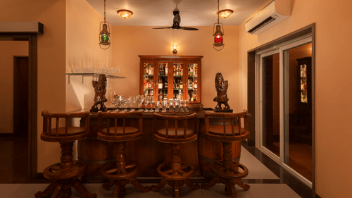 A bar counter with high chairs, a counter and a cupboard with a collection of premium spirits - Highland Sarovar Portico, Sindhudurg