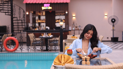 A woman feasting on food at her table next to the swimming pool at Skygrill restaurant with the bar counter in the background