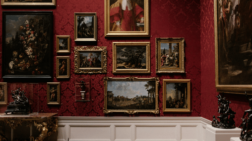 An overview of a museum with many paintings hung on the red wall