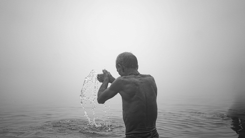 A black and white image of a person taking a bath in a river 