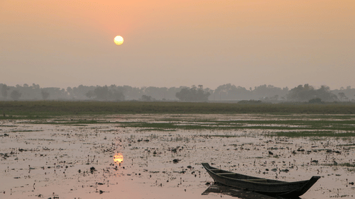 A solitary boat on the shoes of hooghly river with the sun rising in the background