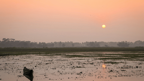 A solitary boat on the shoes of hooghly river with the sun rising in the background