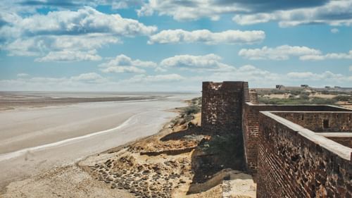 an overview of a river overlapping on the sand with a fort on the side in Gujurat