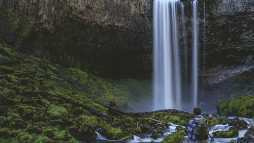 a person sitting on a boulder looking at a waterfall in the distance