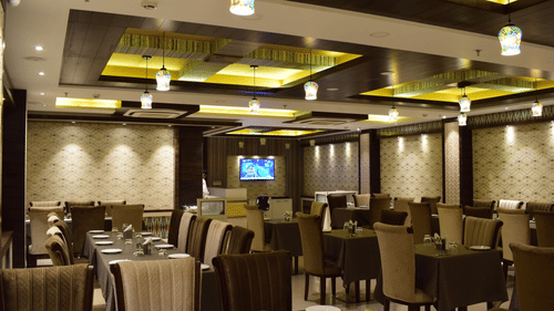 A side view of the dining area at Hotel Uday Palace showcases neatly arranged tables and chairs with warm lighting.