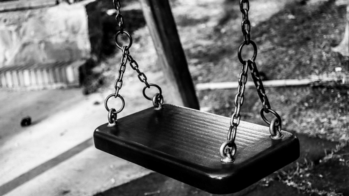 A close black and white shot of a swing in a kid's play area.